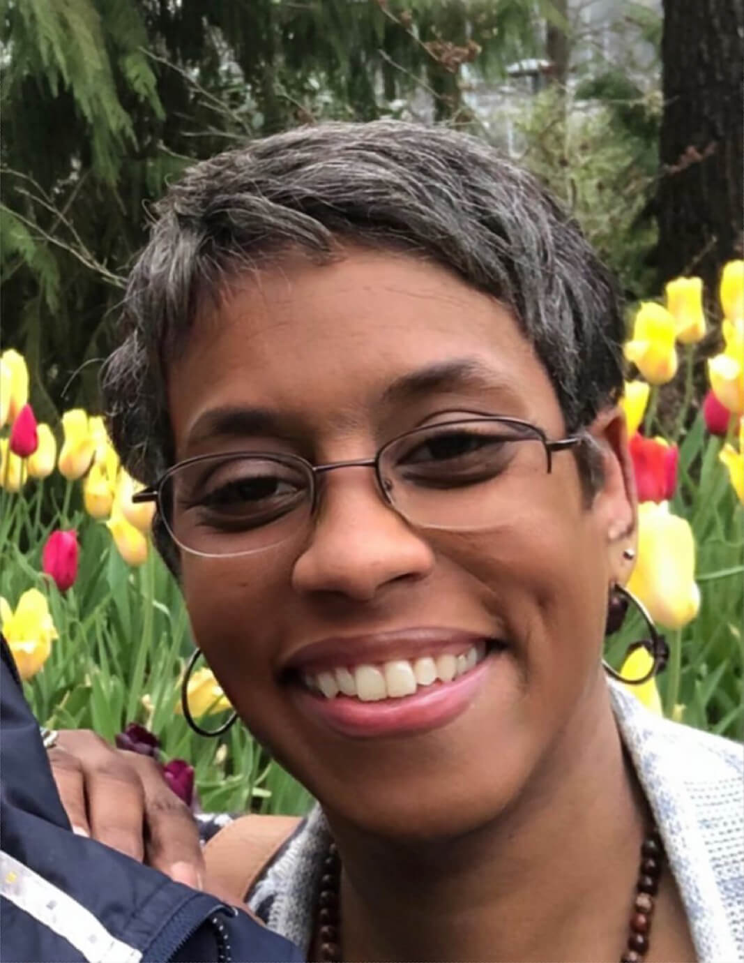 A woman with glasses standing in front of some flowers.