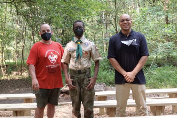 Three men standing in front of a forest.