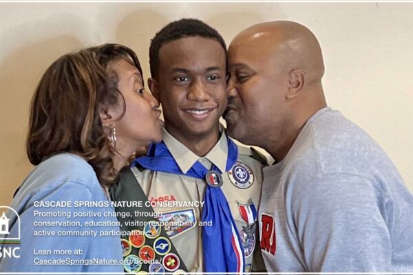 A man and woman kissing on the cheek of a boy scout.