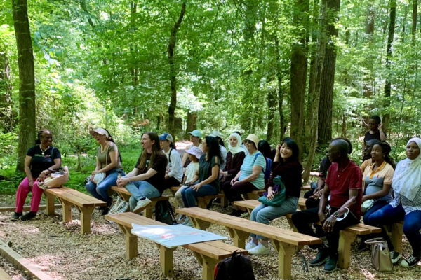 A group of people sitting on wooden benches in the woods.