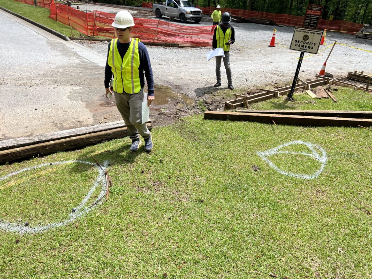 A man in yellow vest standing on grass near two other men.