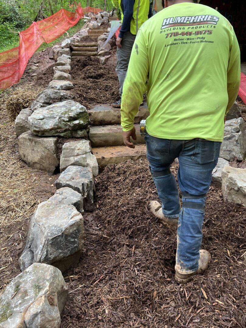 A man in green shirt walking on dirt path.