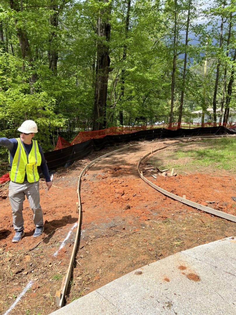 A man in yellow vest standing on dirt road.