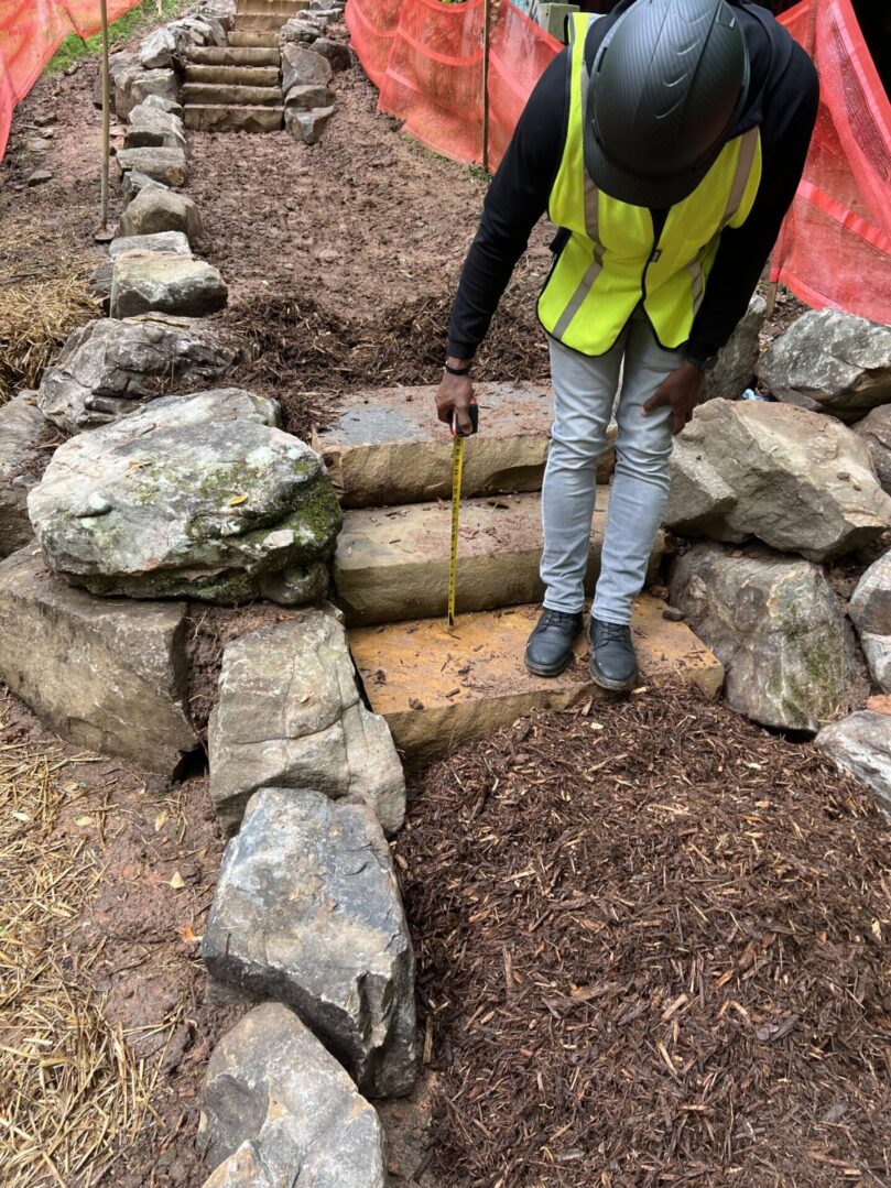 A person in yellow vest standing next to rocks.