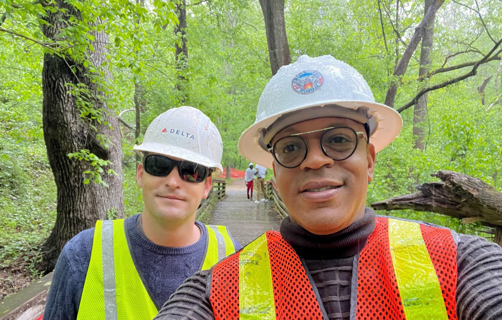 Two men in hard hats and safety vests standing on a path.