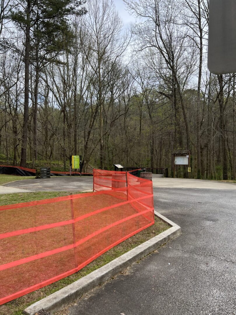 A road with orange fence and trees in the background.