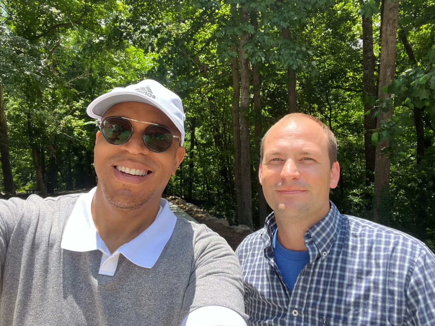 Two men posing for a picture in front of trees.