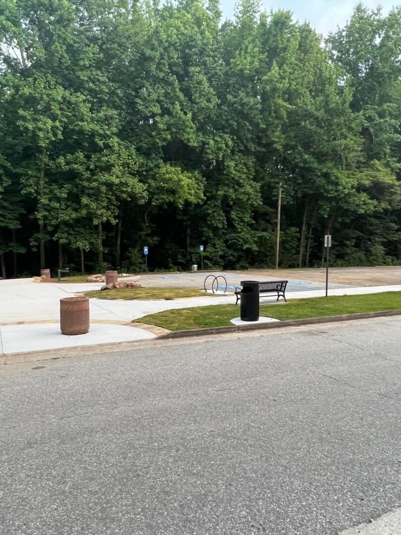 A park with benches and trash cans on the side of road.