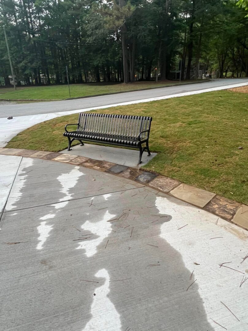 A bench on the side of a sidewalk near grass.