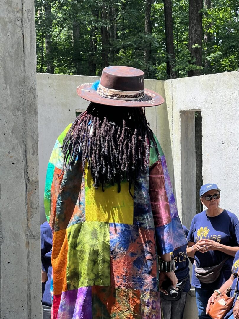 A man with long hair and a hat is standing in front of some people.