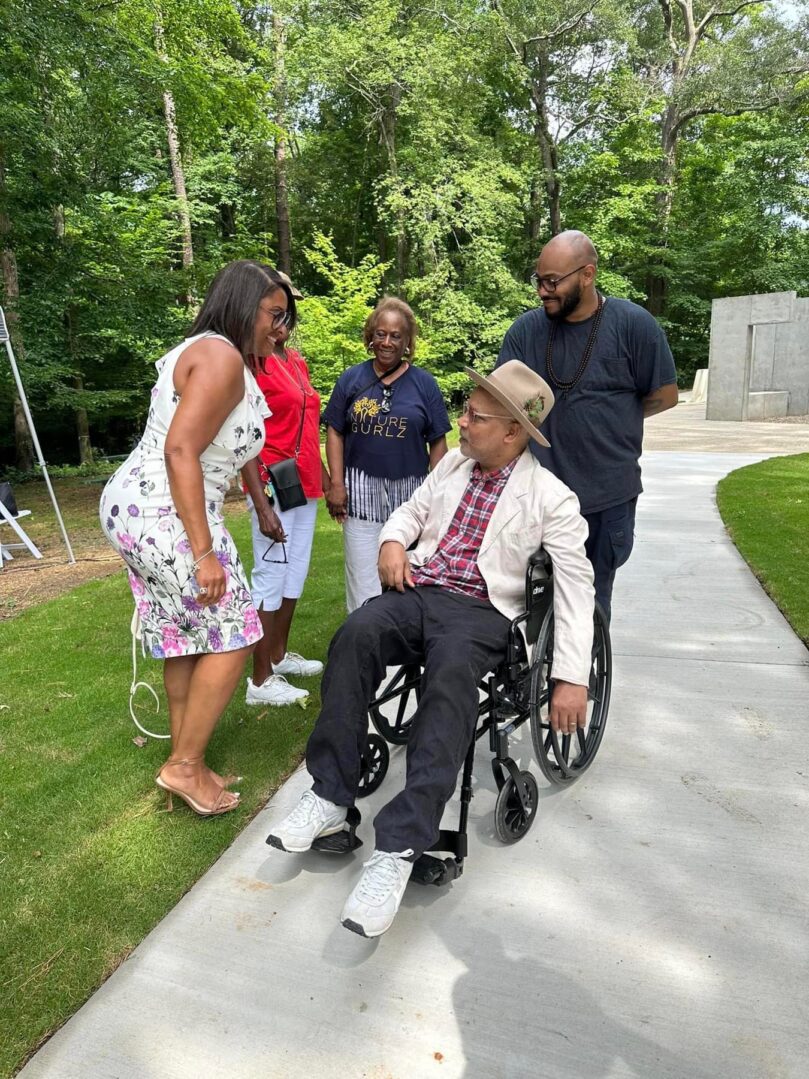 A man in a wheelchair is being pushed by two women.