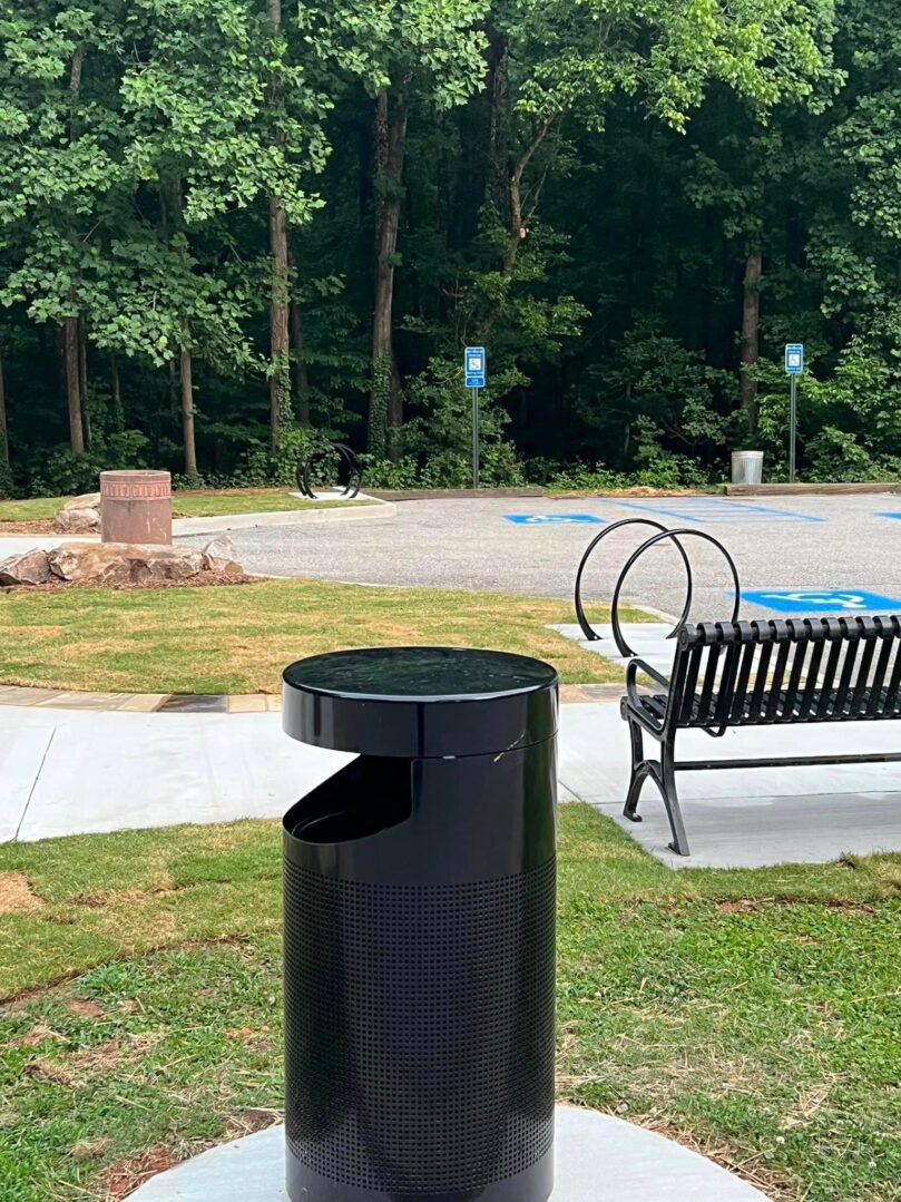 A black trash can in the middle of a park.