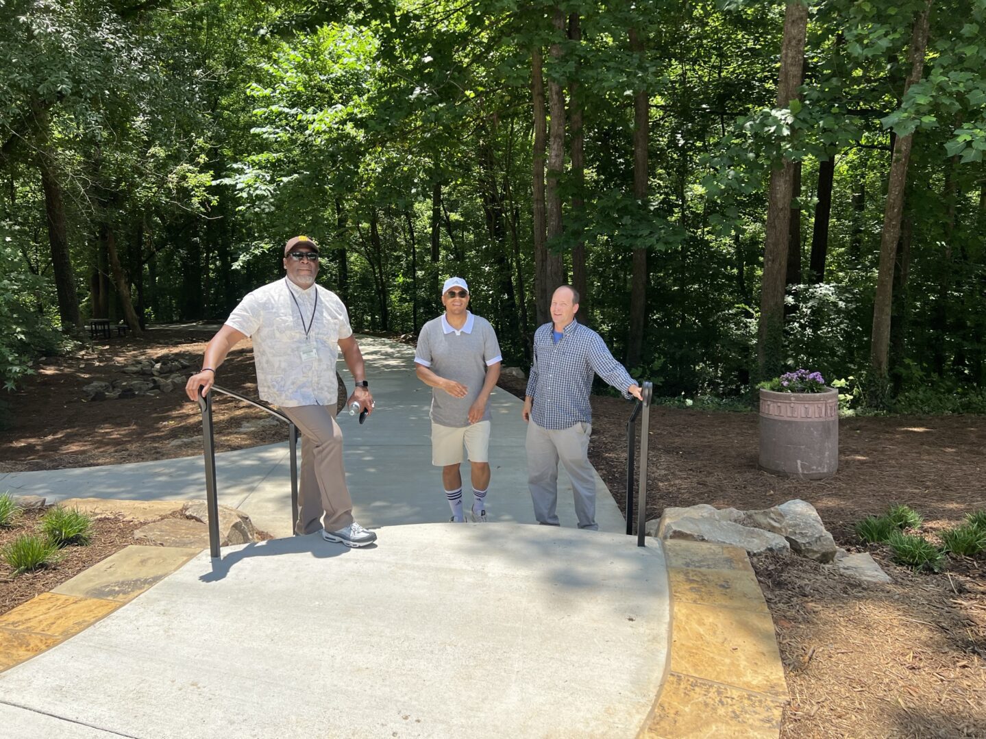 Three men standing on a concrete slab in the woods.