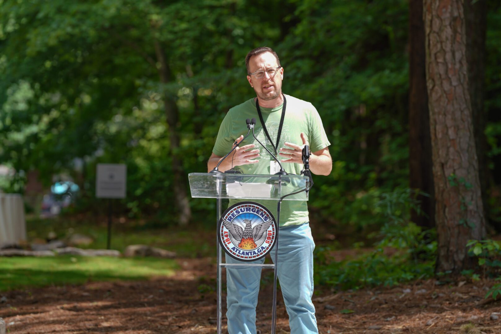 A man standing at a podium in front of trees.