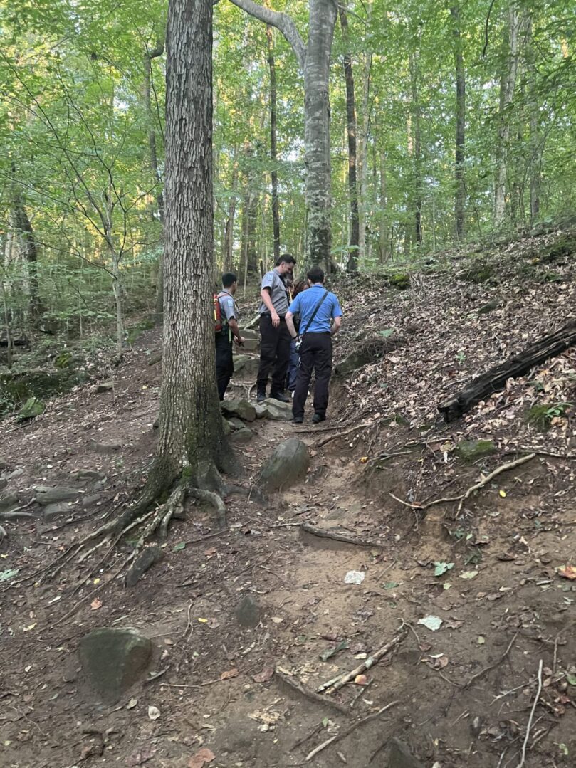 Three people standing on a trail in the woods.